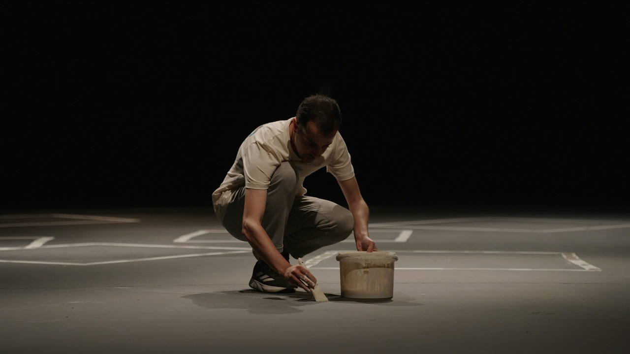 A man paints on the floor in a black room